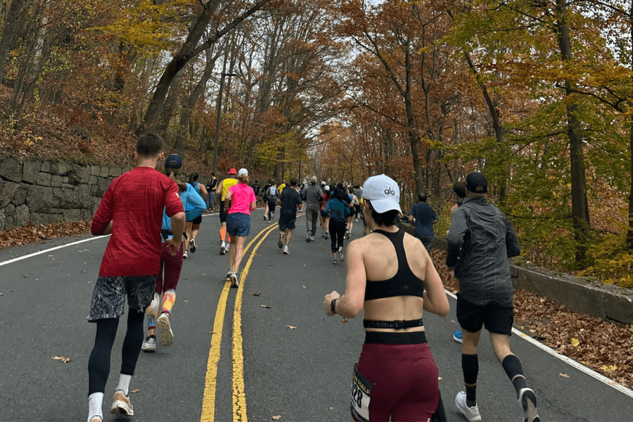 Runners participating in a Thanksgiving Turkey Trot in Boston on a fall morning, wearing race bibs and cold-weather gear.